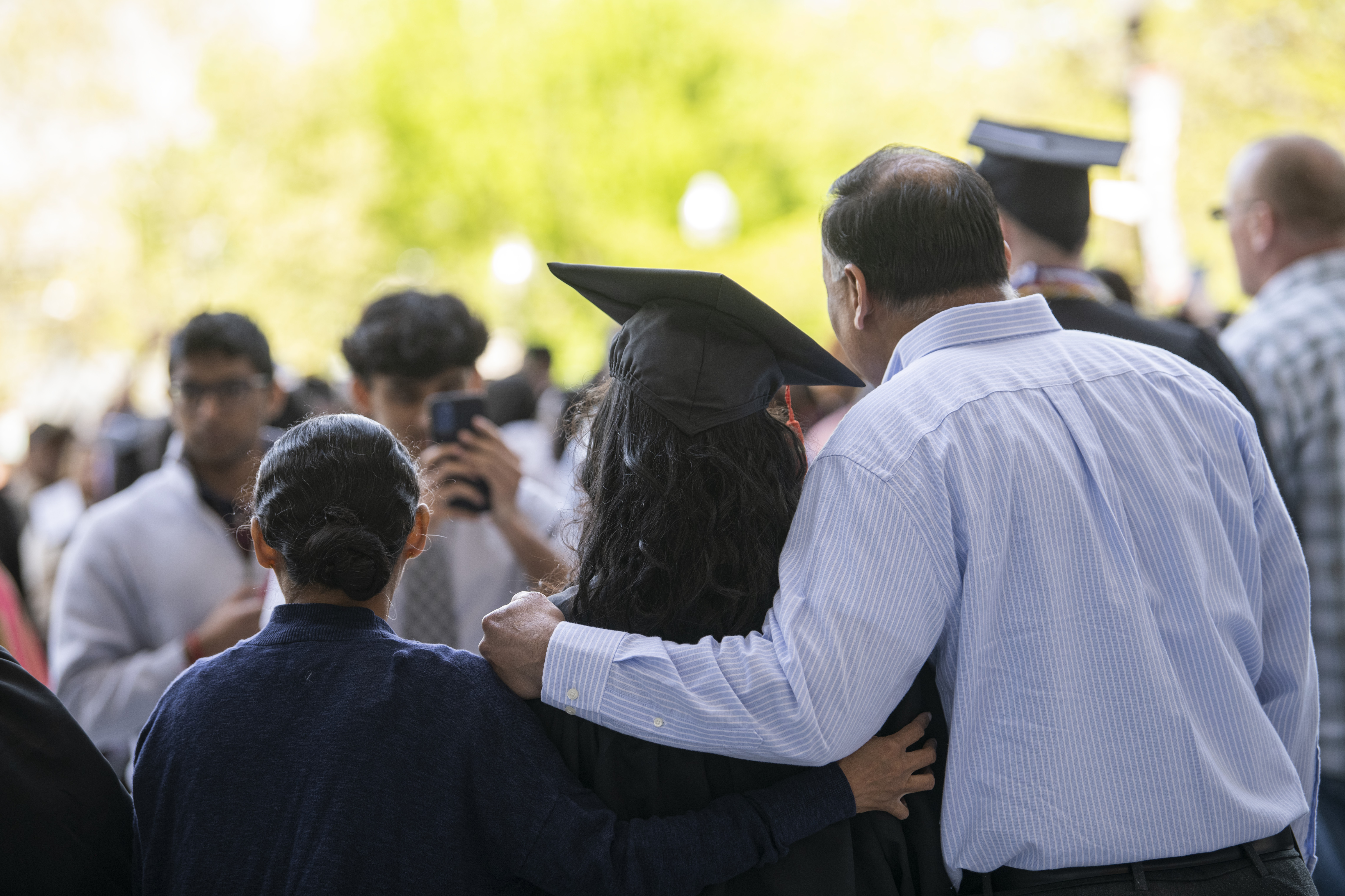 A graduate wearing a cap and gown stands for a picture with their family