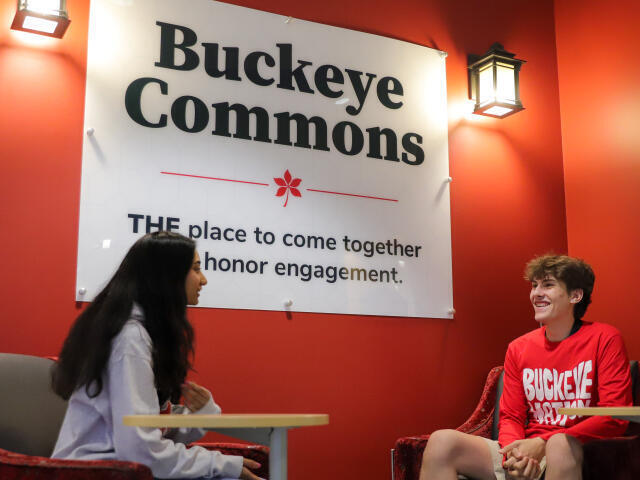 Two students sit outside Buckeye Commons with the office's sign in the background
