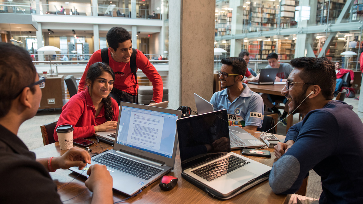 A group of five students work together with laptops on a table inside of Thompson Library