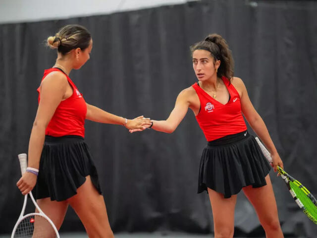 Two women from Ohio State's tennis team exchange high fives while holding tennis rackets